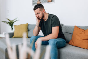 Dark-haired man sitting on a sofa holding his cheek in pain