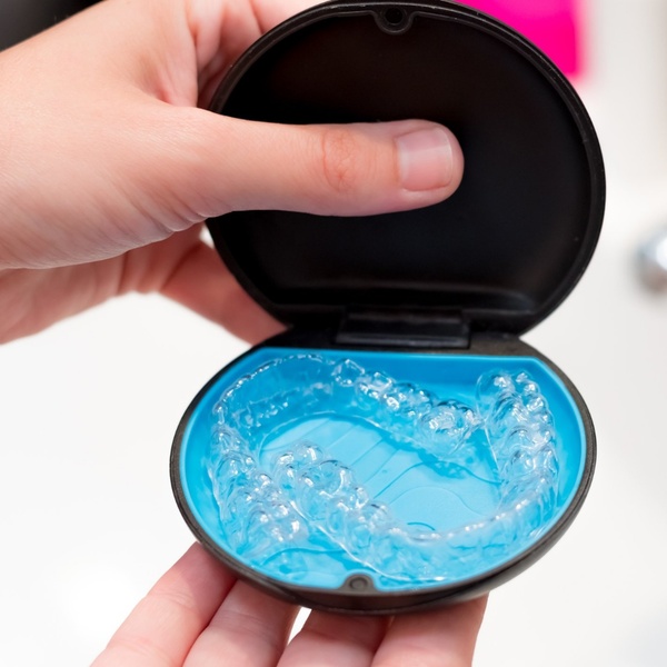 Two hands holding Suresmiles clear aligners with their case on their palms